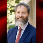 Photo of a man in blue blazer and red tie on a red and black graphic background