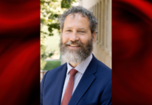 Photo of a man in blue blazer and red tie on a red and black graphic background