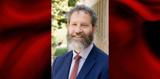 UofL names new dean for School of Public Health and Information Sciences Photo of a man in blue blazer and red tie on a red and black graphic background