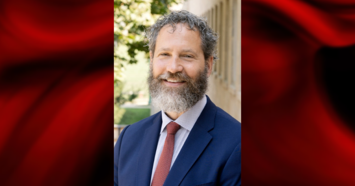 Photo of a man in blue blazer and red tie on a red and black graphic background