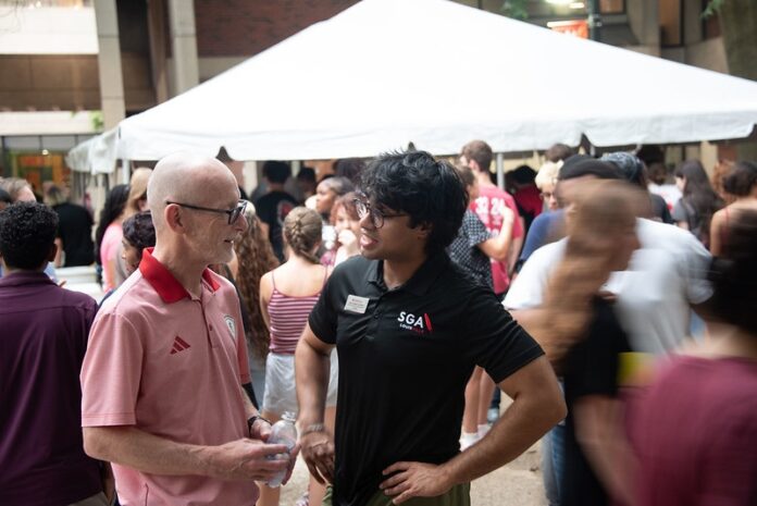 Bradley at Welcome Week picinic 26 - 3 Two men talking with a large white tent and people walking in the background.