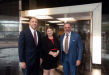 Two men in business suits and a woman in a black dress with red trim.