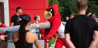 Louie the Cardinal bird mascot helps push items in a large bin into a residence hall.
