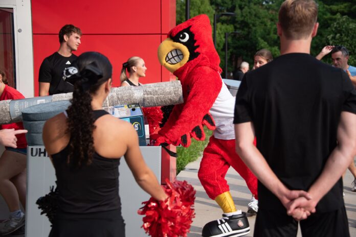 Louie Move In_1042 Louie the Cardinal bird mascot helps push items in a large bin into a residence hall.
