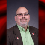 UofL names Charlie Perusse as inaugural chief transformation officer Portrait of a man wearing a green shirt in a red and black graphical template