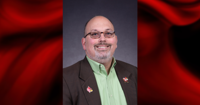 Charlie Perusse - UofL News template Portrait of a man wearing a green shirt in a red and black graphical template