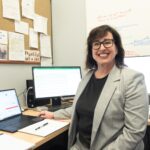 Smiling woman seated at desk surrounded by four computers