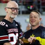 UofL recognized for outstanding support of military community Man in football jersey receives baton from Golden Knight