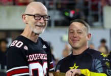 UofL recognized for outstanding support of military community Man in football jersey receives baton from Golden Knight