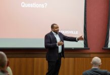Darrell Clark speaks with his hands animated in front of a screen that states "Questions?"