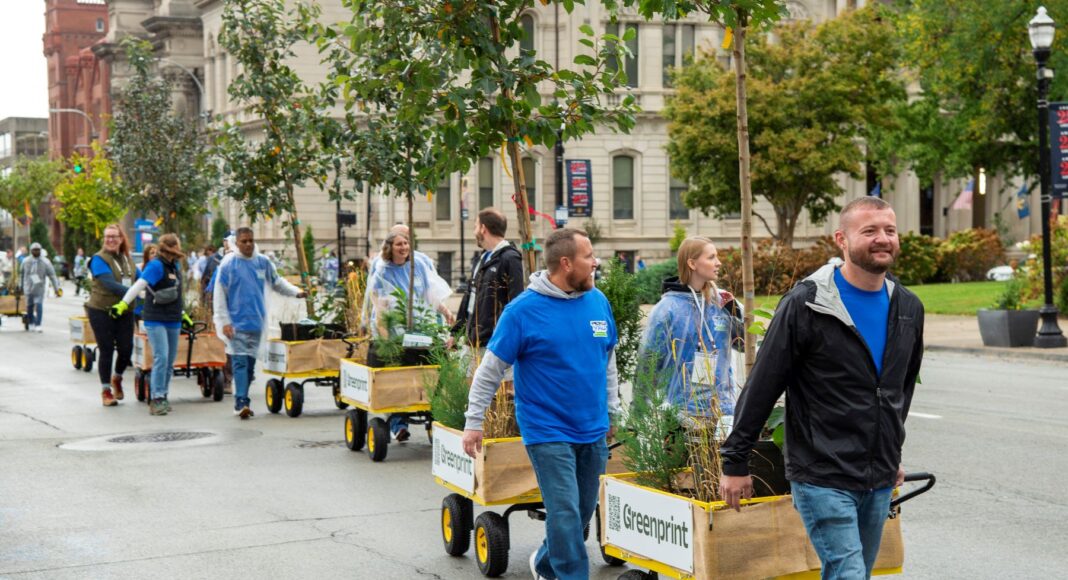 Moving forest helps Louisvillians see how trees can enhance the city People pull wagons with trees and shrubs on the street.